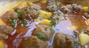 Savory spiced meatball stew with potatoes, garnished with fresh herbs in a rich, flavorful broth.